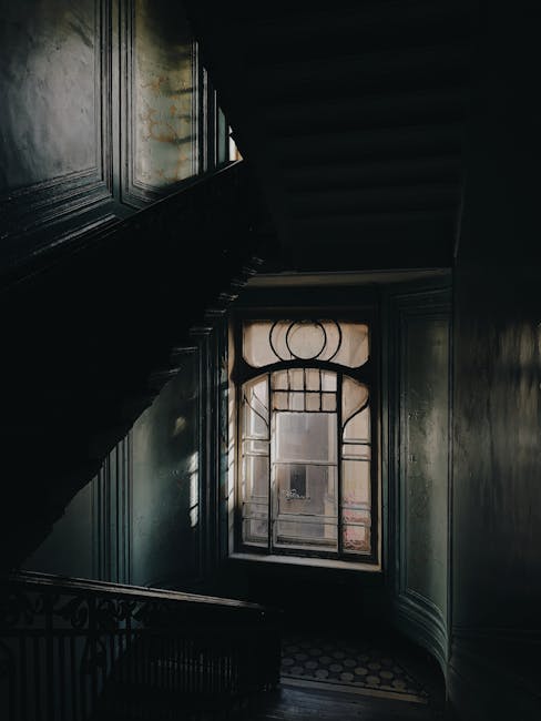 A long, covered Victorian-style porch with white-painted wooden columns and ceiling, featuring black wrought iron fencing in the foreground. Overhead lantern-style lights hang along the corridor, whic