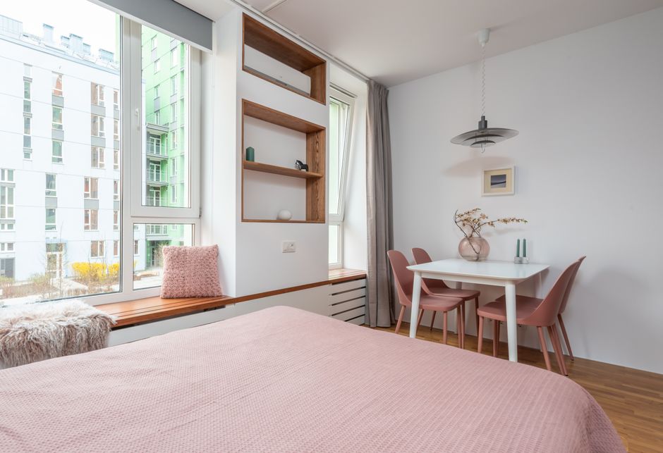 Interior view of a living room during a house removal process, featuring large windows with sheer white curtains and beige drapes allowing natural light, a grey upholstered sofa with plush cushions, a